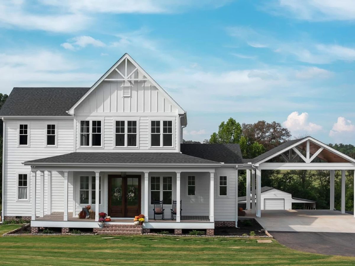 White two-story farmhouse with a front porch and attached carport